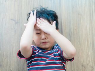 Afbeelding van een jongetje dat het hoofd vastpakt omdat het hoofdpijn heeft door een hersenschudding.